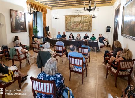 fotografia. spotkanie literacki środek europy w ramach festiwalu art piknik w willi decjusza. goście siedzą przy długim stole w sali marceliny czartoryskiej. na pierwszym planie publiczność siedząca na krzesłach.